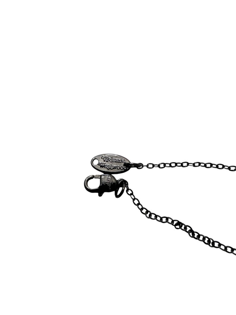 May include: A dark gunmetal-toned necklace chain featuring a lobster claw clasp and an oval-shaped metal tag engraved with the text Vivienne Westwood. The chain consists of small, uniform circular links connected to the secure fastening mechanism.