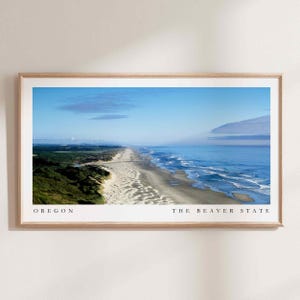 Op de afbeelding: Een panoramisch uitzicht op een zandstrand met blauwe oceaan golven die breken op de kust. Groene duinen en vegetatie zijn zichtbaar op de voorgrond. De tekst "OREGON THE BEAVER STATE" is gedrukt onderaan de afbeelding.