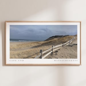 May include: A panoramic view of a sandy beach with a wooden fence leading to a dune. The ocean is in the background with waves crashing on the shore. The text "CAPE COD MASSACHUSETTS" is at the bottom of the image.