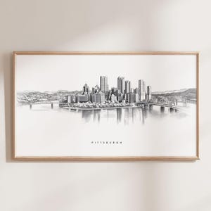 May include: A black and white pencil drawing of the Pittsburgh skyline, featuring the city's iconic skyscrapers and bridges. The drawing is framed in a light wood frame and the word "PITTSBURGH" is printed below the image.