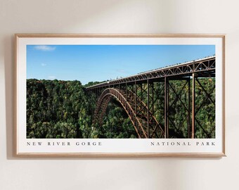 Könnte beinhalten: Gerahmter Druck der New River Gorge Bridge in West Virginia. Die Brücke ist rostbraun und überspannt einen grünen Wald unter blauem Himmel. Der Text "NEW RIVER GORGE NATIONAL PARK" ist unten im Bild aufgedruckt.
