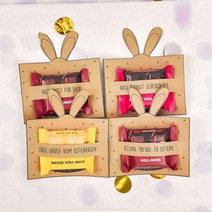 May include: Four Easter gift boxes with chocolate bars. Each box is brown with bunny ears cut out at the top. The boxes contain chocolate bars with German text.