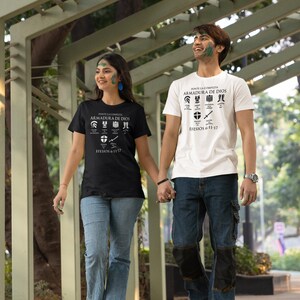 Puede incluir: Una pareja lleva camisetas negras y blancas con el texto "PONTE LA COMPLETA ARMADURA DE DIOS" y "EFESIOS 6:11-17". La pareja camina de la mano por un camino pavimentado.