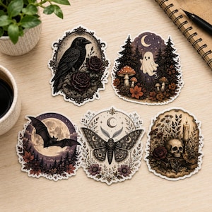 May include: Five die-cut stickers featuring dark illustrations: a raven in an ornate frame, a ghost in a forest with mushrooms, a bat flying before a full moon, a moth with floral accents and a crescent moon, and a skull with a candle and flowers.