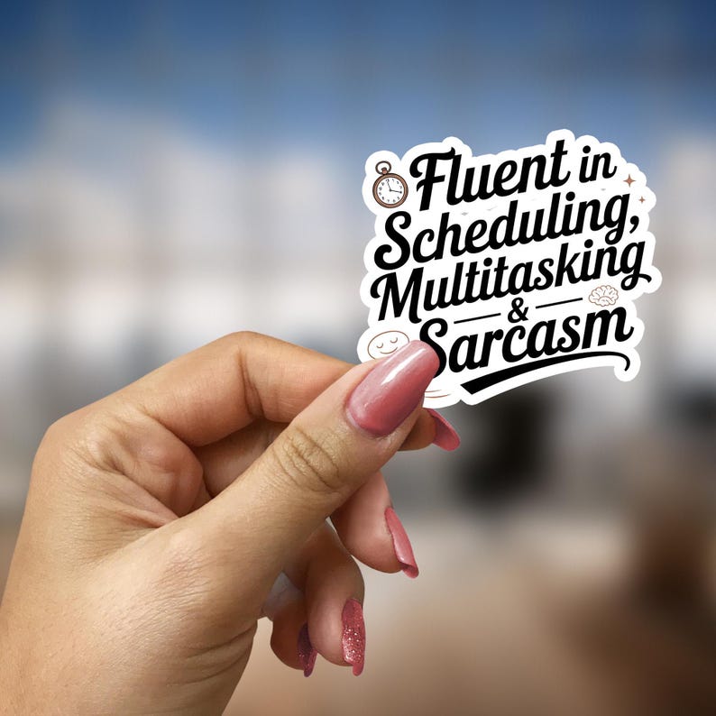 May include: A white sticker with the text "Fluent in Scheduling, Multitasking & Sarcasm" in a black, stylized font. The sticker is held by a hand with pink nail polish against a blurred background.