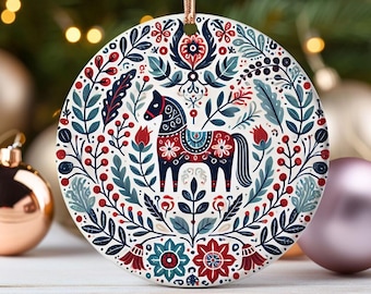 May include: A round, white ornament with a red, blue, and green floral pattern. A stylized horse with a red, blue, and white saddle is in the center of the ornament.
