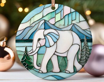 May include: A stained glass ornament featuring a white elephant with blue and pink accents standing in a green field with a blue mountain range in the background.