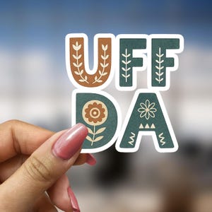 May include: A sticker with the words "UFF DA" in a stylized font. The letters are green with brown accents and floral designs.