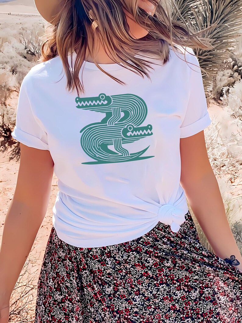 Peut inclure: T-shirt blanc avec un motif vert de deux alligators stylis&eacute;s se faisant face.