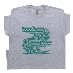 Peut inclure: Un t-shirt gris avec un motif turquoise de deux alligators stylis&eacute;s superpos&eacute;s.