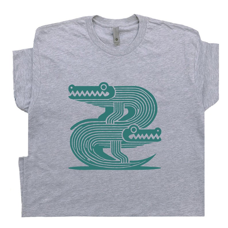 Peut inclure: Un t-shirt gris avec un motif turquoise de deux alligators stylis&eacute;s superpos&eacute;s.