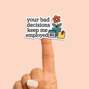 May include: White sticker with the text "your bad decisions keep me employed" in black. The sticker also features a red flower in a blue pot, a calendar, and a yellow sticky note.