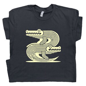 Peut inclure: Un t-shirt bleu marine fonc&eacute; avec un motif graphique de deux alligators stylis&eacute;s en jaune clair.