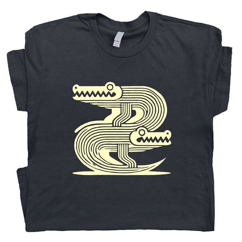 Peut inclure: Un t-shirt bleu marine fonc&eacute; avec un motif graphique de deux alligators stylis&eacute;s en jaune clair.