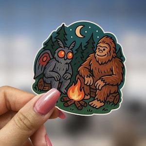 Puede incluir: Una pegatina con una polilla de dibujos animados y un Bigfoot de dibujos animados sentados alrededor de una fogata en un entorno de bosque. La polilla es gris con ojos rojos y el Bigfoot es marr&oacute;n con una gran sonrisa.