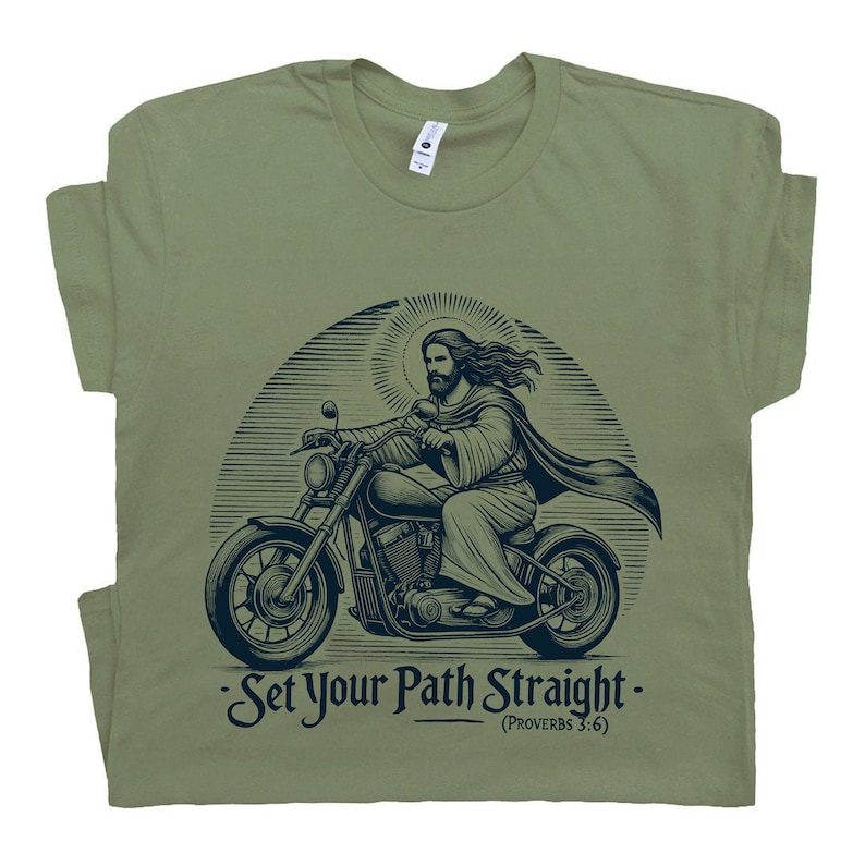 Puede incluir: Una camiseta verde con un gr&aacute;fico de Jes&uacute;s conduciendo una motocicleta. El gr&aacute;fico es en blanco y negro y tiene un aspecto vintage. El texto en la camiseta dice "Set Your Path Straight - (Proverbs 3:6)"