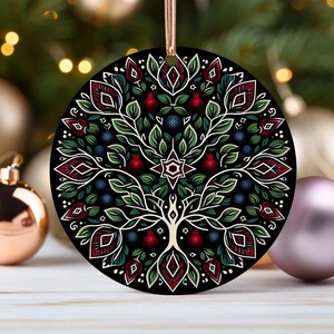 May include: A round, black ornament with a white tree of life design. The tree is surrounded by red pomegranates and blue berries. The ornament has a red and white geometric pattern around the edge.