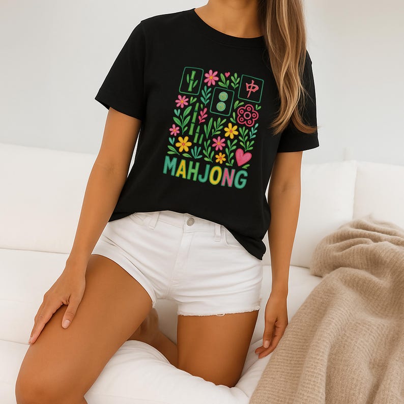 May include: Black t-shirt with a colorful floral and Mahjong tile design. The design includes flowers, hearts, and the word "MAHJONG" in a gradient font. The shirt is paired with white shorts.