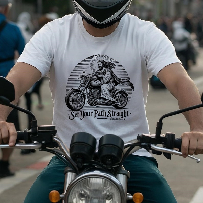 Puede incluir: Una camiseta blanca con una ilustraci&oacute;n en blanco y negro de Jes&uacute;s conduciendo una motocicleta. El texto en la camiseta dice "Set Your Path Straight - (Proverbs 3:6)"