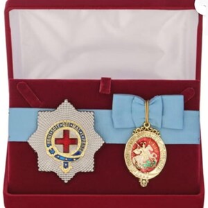 May include: A red velvet box containing two gold medals. One medal features a red cross and the other depicts a knight on horseback.