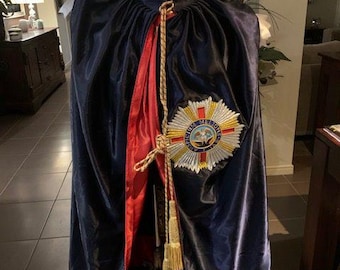 May include: A navy blue satin robe with a red and gold sash and a gold embroidered badge featuring a crown and the words "Virtue Merit" and "Victoria" on a white background.