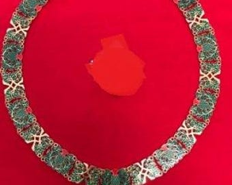 May include: A gold chain with green and red enamel accents. The chain is decorated with a repeating pattern of stylized leaves. A small pendant hangs from the bottom of the chain.