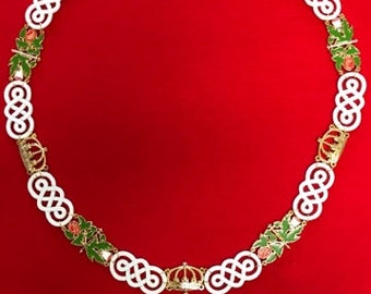 May include: A white and gold chain with a pendant featuring a green and red floral design. The chain is made of interlocking circles and has small crowns and floral accents.