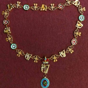 Puede incluir: Una cadena de oro con un colgante que presenta un arpa y una corona. La cadena está decorada con lazos dorados, arpas y círculos de esmalte rojo, blanco y verde.