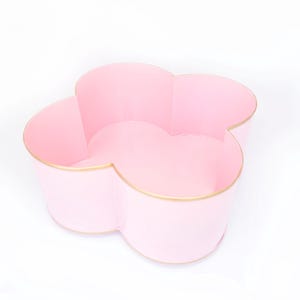 May include: A pink flower-shaped bowl with a gold rim. The bowl is made of ceramic and has a smooth, glossy finish.
