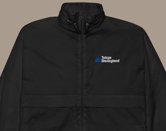 May include: A black zip-up windbreaker jacket featuring a high collar with a drawstring, long sleeves with elastic cuffs, and a drawstring hem. The chest displays a blue and white logo with the text Tokyo Disneyland printed on it.