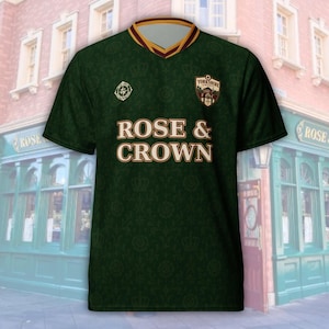 May include: A dark green short-sleeve V-neck shirt featuring a repeating crown and floral pattern. The chest displays the text ROSE & CROWN in white lettering, a circular compass logo, and a shield-shaped crest labeled YORKSHIRE COUNTY FC.