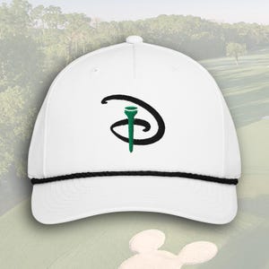Op de afbeelding: Witte golfpet met een zwarte touwrand en een groen en zwart geborduurd logo. Het logo toont een golftee in een gestileerde letter "D". De pet heeft een gebogen klep en een knoop aan de bovenkant.
