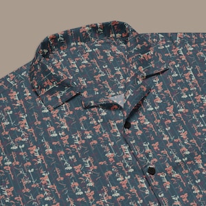 May include: A short-sleeved button-down shirt with a dark teal background and a repeating floral pattern in coral and white. The shirt has a classic collar and black buttons.