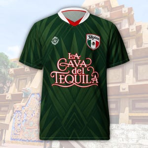 May include: A dark green short-sleeve jersey with a V-neck collar featuring white and red trim. The front displays the text LA CAVA del TEQUILA in white script and block lettering, a Mexico crest, and a compass rose emblem on a leaf pattern.