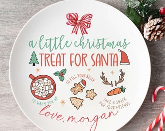 May include: White ceramic plate with a festive Christmas design. It says "a little christmas treat for santa" with illustrations of a gingerbread man, a cup of hot chocolate with marshmallows, a carrot, and a Christmas tree. The plate is signed "love, morgan".