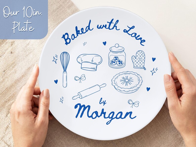 May include: A white ceramic plate, 10 inches in diameter, with blue illustrations of baking tools and the words "Baked with Love by Morgan." The plate features a whisk, chef's hat, jar, oven mitt, pie, and rolling pin.