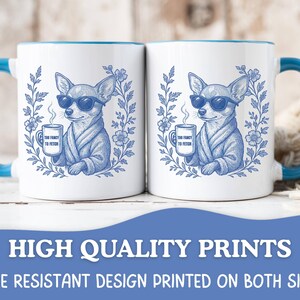 May include: Two white coffee mugs with blue handles and rims. Each mug features a blue illustration of a chihuahua wearing sunglasses and a robe, holding a mug that says "Too Fancy to Fetch". The mugs are surrounded by a floral wreath.
