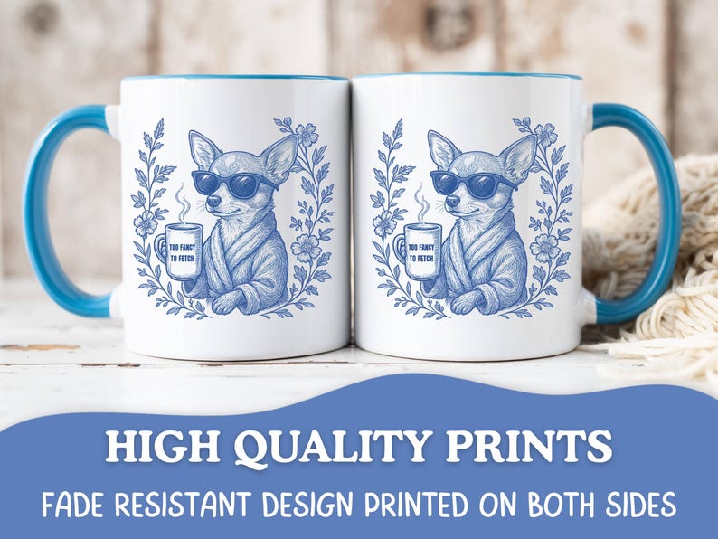 May include: Two white coffee mugs with blue handles and rims. Each mug features a blue illustration of a chihuahua wearing sunglasses and a robe, holding a mug that says "Too Fancy to Fetch". The mugs are surrounded by a floral wreath.