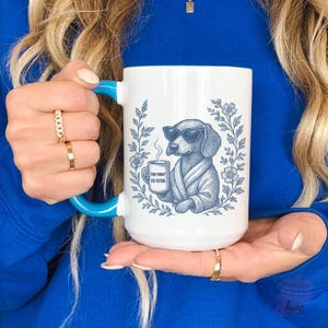 May include: White ceramic mug with a blue handle and rim. The mug features a blue illustration of a dachshund wearing sunglasses and a robe, holding a coffee cup. The text on the cup reads "TOO FANCY TO FETCH".