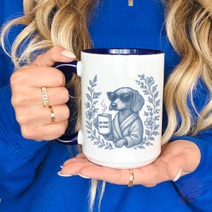 May include: White ceramic mug with a blue interior and handle. The mug features a detailed illustration of a dachshund wearing sunglasses and a robe, holding a coffee cup. Text on the cup reads "Too Fancy to Fetch". The design is surrounded by floral elements.