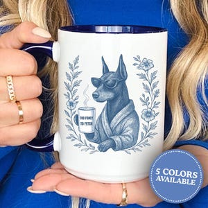 May include: White ceramic mug with a blue interior and handle. The mug features a blue illustration of a dog wearing sunglasses and a robe, holding a coffee cup. The cup reads "Too Fancy to Fetch". A blue floral wreath surrounds the dog. A button on the mug says "5 Colors Available".
