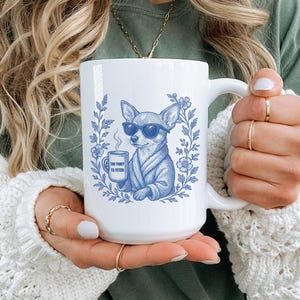May include: White ceramic mug featuring a blue illustration of a chihuahua wearing sunglasses and a robe, holding a coffee cup. The mug has the text "Too Fancy to Fetch" and is surrounded by floral elements.