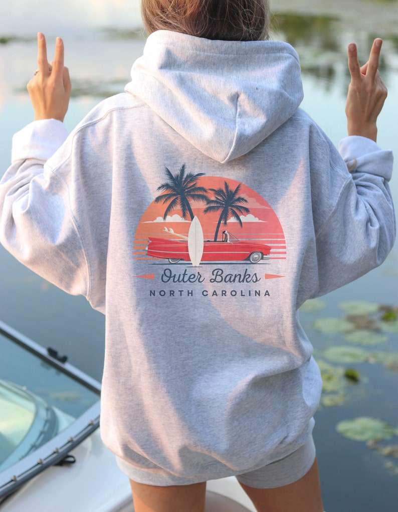 May include: Gray hooded sweatshirt with a graphic print of a red car driving on a beach with palm trees and a surfboard. The text "Outer Banks North Carolina" is printed below the graphic.