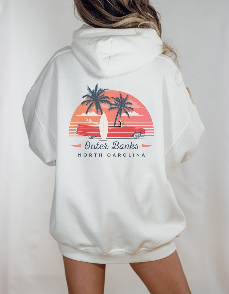 May include: White hooded sweatshirt with a graphic print of a red car, surfboard, and palm trees against a sunset background. The text "Outer Banks North Carolina" is printed below the graphic.