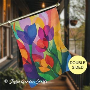 May include: A rectangular garden flag featuring a vibrant, abstract floral design with overlapping translucent shapes in shades of blue, purple, red, orange, yellow, and green. A yellow circular badge on the right reads DOUBLE SIDED.