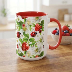 Peut inclure: Mug en céramique blanche avec intérieur et anse rouges. Le mug est orné d'un motif de fraises rouges, de fleurs blanches, de feuilles vertes et de coccinelles rouges. Le mug est posé sur une surface en bois.
