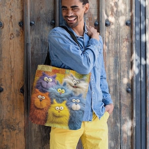 May include: A colorful tote bag featuring a group of cartoon cats with fluffy fur in shades of orange, purple, yellow, and blue. The bag has a black strap and a patterned background.