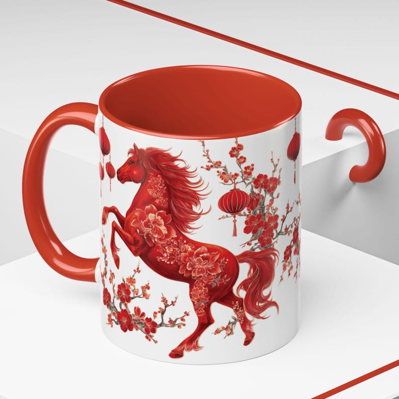 May include: A white ceramic mug with a red interior and handle. The mug features a red horse design with floral accents and hanging lanterns, set against a white background. The design is likely inspired by Asian art.