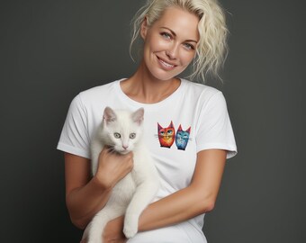 May include: A woman wearing a white t-shirt with a colorful cat graphic holds a white cat in her arms. The cat is looking at the camera.