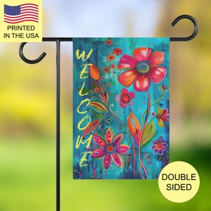 May include: A rectangular garden flag featuring a vibrant teal background with painted floral motifs in shades of pink, orange, and red. The word WELCOME is written vertically in yellow text on the left side. The flag hangs on a black metal stand.